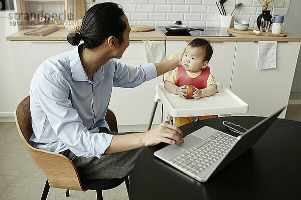 Freelancer father stroking daughter sitting on high chair at home