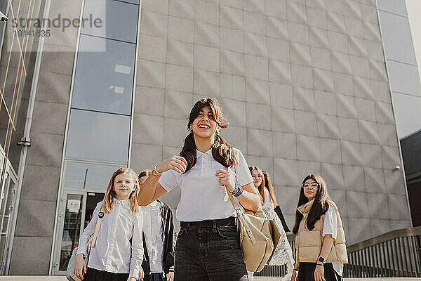 Smiling girl with school friends standing in front of building