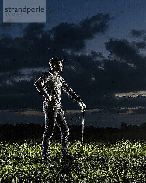 Mann mit der Hand auf der Hüfte steht auf Gras und hält einen Golfschläger