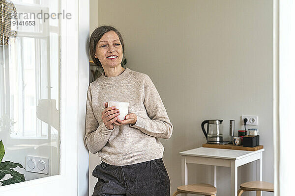 Smiling woman standing with coffee cup at home
