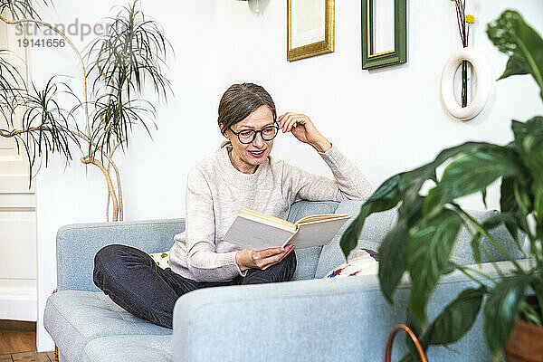 Mature woman wearing eyeglasses reading book