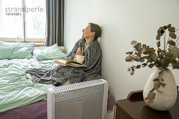 Nachdenkliche Frau mit Decke sitzt zu Hause im Bett