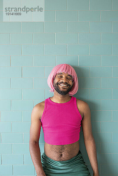 Lächelnder junger queerer Mann steht vor einer gefliesten Wand