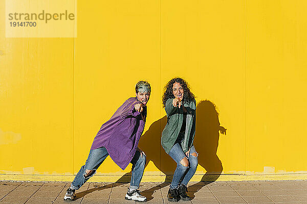 Glückliches lesbisches Paar tanzt vor gelber Wand