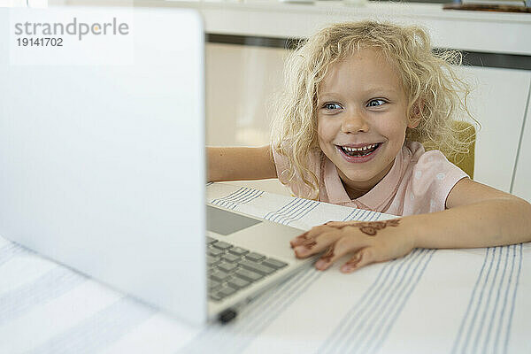 Lächelndes Mädchen  das zu Hause einen Laptop auf dem Tisch benutzt
