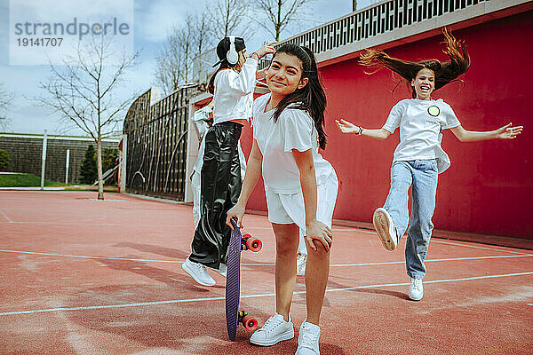 Lächelndes Teenager-Mädchen mit Skateboard auf dem Spielplatz