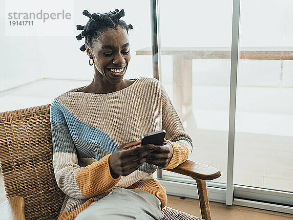 Smiling woman using mobile phone in chair at home