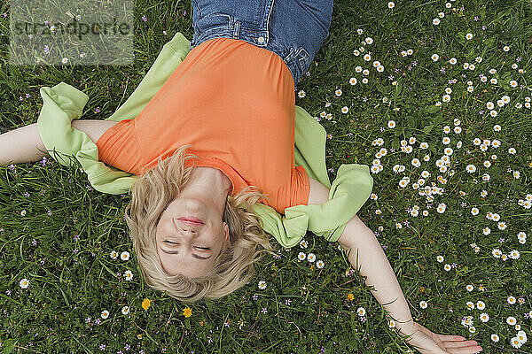 Smiling woman with eyes closed lying amidst flowers on grass