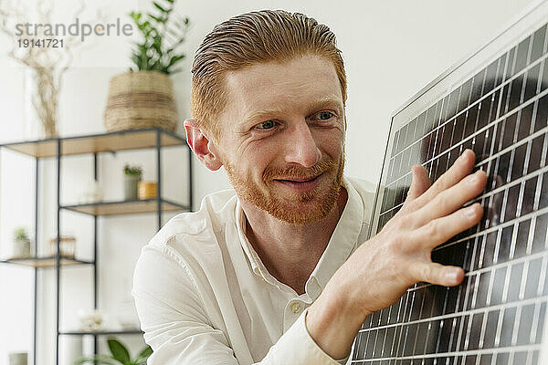 Glücklicher Geschäftsmann untersucht Solarpanel im Büro