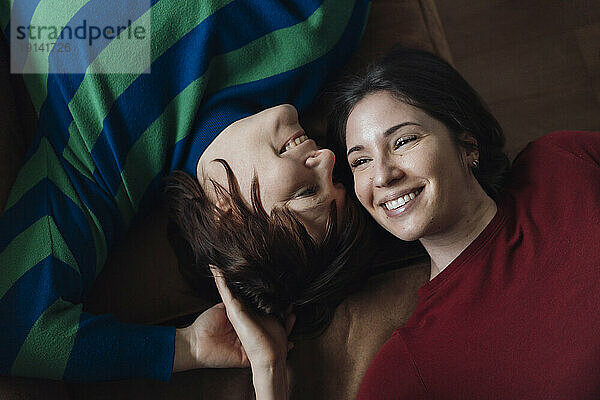 Smiling lesbian couple lying down on sofa at home