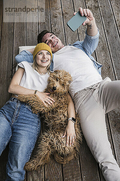 Glückliches junges Paar macht Selfie mit Hund und liegt auf dem Boden