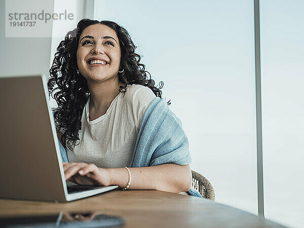 Cheerful woman looking up and using laptop at table