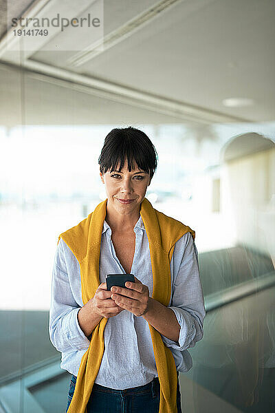 Selbstbewusste Geschäftsfrau hält Smartphone vor Glaswand