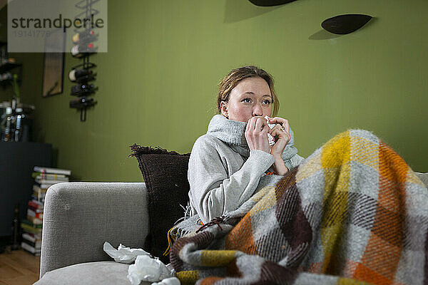 Sick young woman blowing nose with tissue relaxing on couch