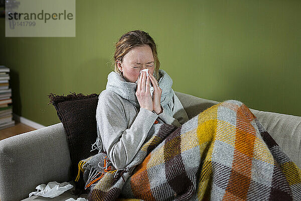 Sick young woman sneezing in tissue relaxing on couch