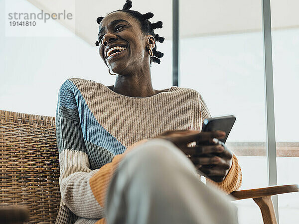 Cheerful woman holding smartphone sitting in armchair