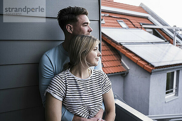 Lächelndes junges Paar lehnt an der Wand auf dem Balkon