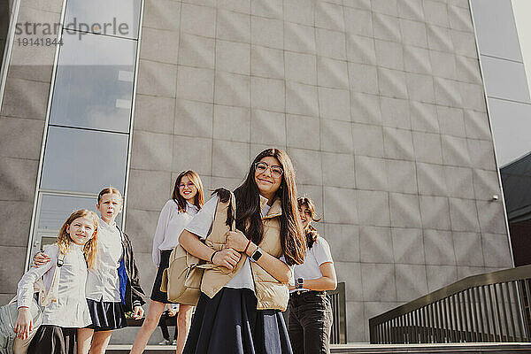 Lächelndes Mädchen mit Schulfreunden  die vor dem Gebäude stehen