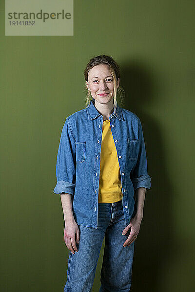 Selbstbewusste junge Frau im Jeanshemd steht vor einer grünen Wand