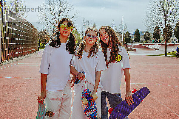 Lächelnde Teenager-Freunde mit Skateboard stehen auf dem Spielplatz