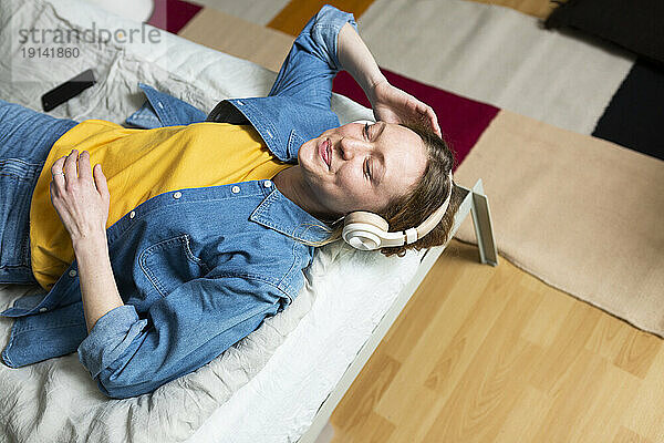 Young woman enjoying music with headphones lying on bed