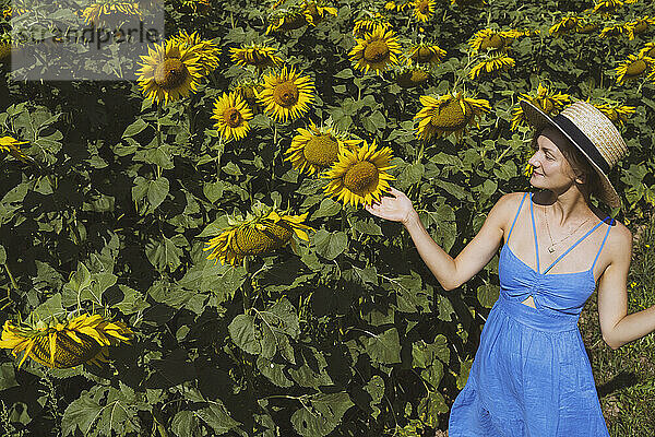 Smiling woman touching sunflowers in field