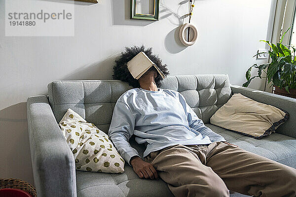 Mann mit Buch im Gesicht schläft zu Hause auf dem Sofa