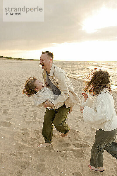 Fröhlicher Vater  der Spaß mit Töchtern am Strand hat
