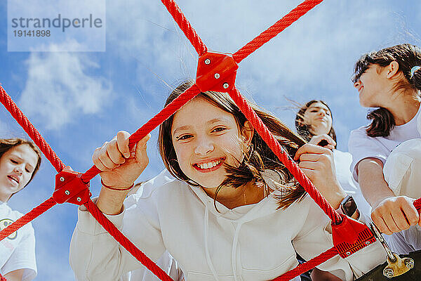 Glückliches Teenager-Mädchen mit Freunden  die im Klettergerüst auf dem Spielplatz spielen