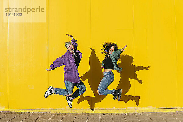 Fröhliches lesbisches Paar springt vor gelbe Wand