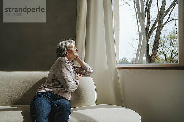 Reife Frau entspannt sich zu Hause auf der Couch am Fenster