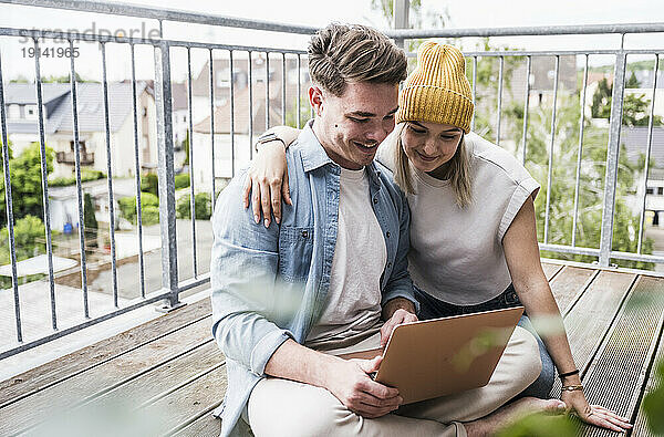 Glückliches Paar benutzt Laptop auf Balkon