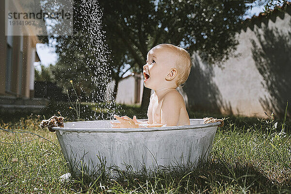 Baby boy looking at water in bathtub at backyard
