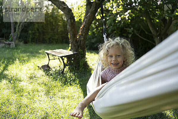 Glückliches Mädchen sitzt auf Hängematte im Garten