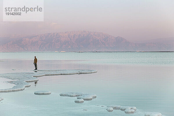 Mann steht bei Sonnenuntergang auf Salzformationen vor dem Berg
