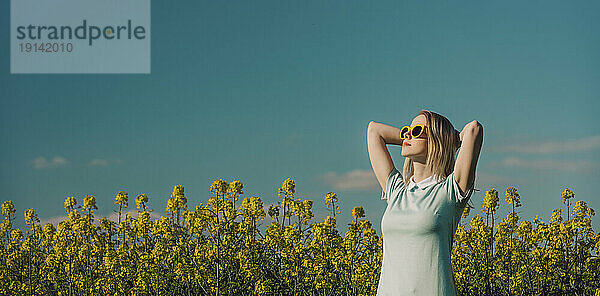 Frau mit den Händen hinter dem Kopf steht an einem sonnigen Tag im Feld