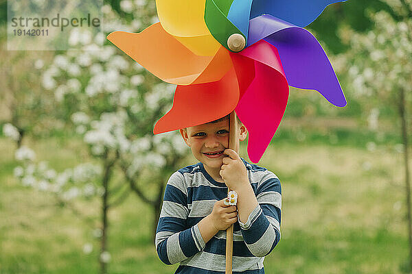 Fröhlicher Junge mit Windradspielzeug steht im Garten