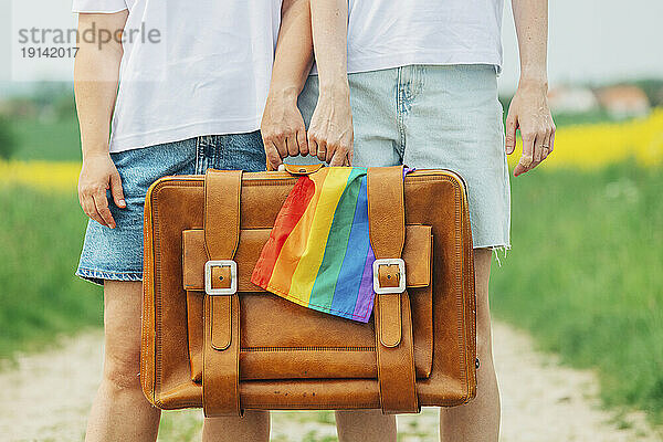 Lesben halten Koffer mit Regenbogenfahne in der Hand