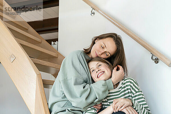 Zärtliche Mutter umarmt Tochter  die zu Hause auf Stufen sitzt