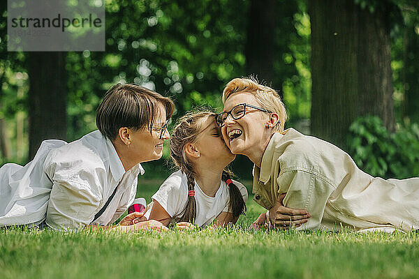 Daughter kissing lesbian mother lying on grass at park