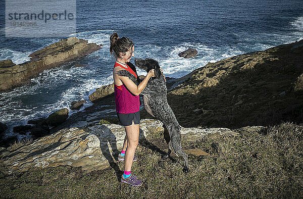 Frau steht mit Hund auf Felsen am Meer