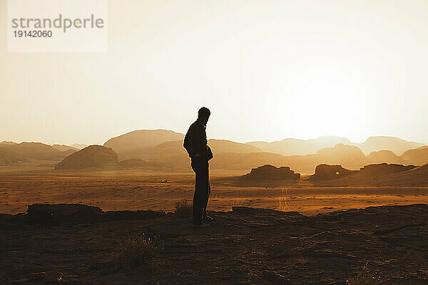 Young man standing in desert and looking at sunset