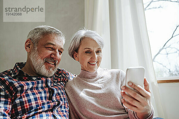 Lächelndes reifes Paar bei einem Videoanruf über das Smartphone zu Hause