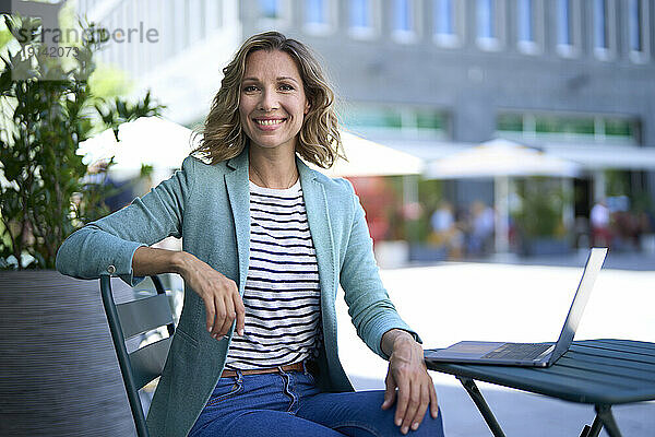 Lächelnde Geschäftsfrau sitzt auf einem Stuhl im Straßencafé