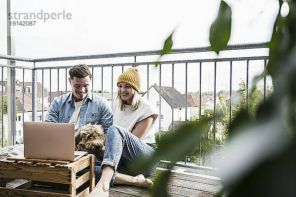 Glückliches junges Paar sitzt mit Hund und benutzt Laptop