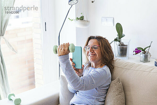 Frau fotografiert zu Hause per Smartphone eine Hand  die eine Hantel hält