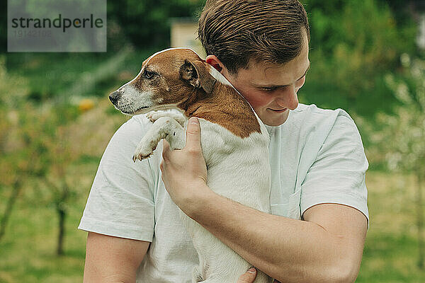 Glücklicher Mann umarmt Jack-Russell-Terrier-Hund im Garten