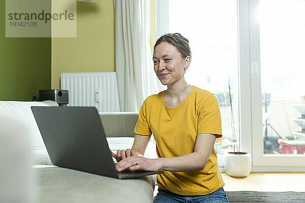 Freiberufler im gelben T-Shirt arbeitet zu Hause mit Laptop