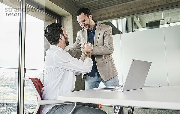 Business colleagues holding hands with laptop at table