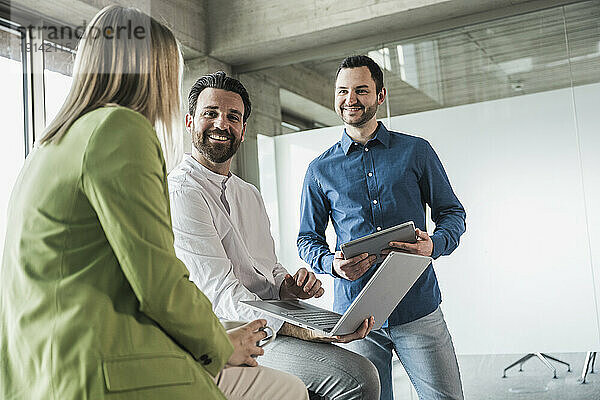 Lächelnder Geschäftsmann mit Kollegen  die am Arbeitsplatz diskutieren